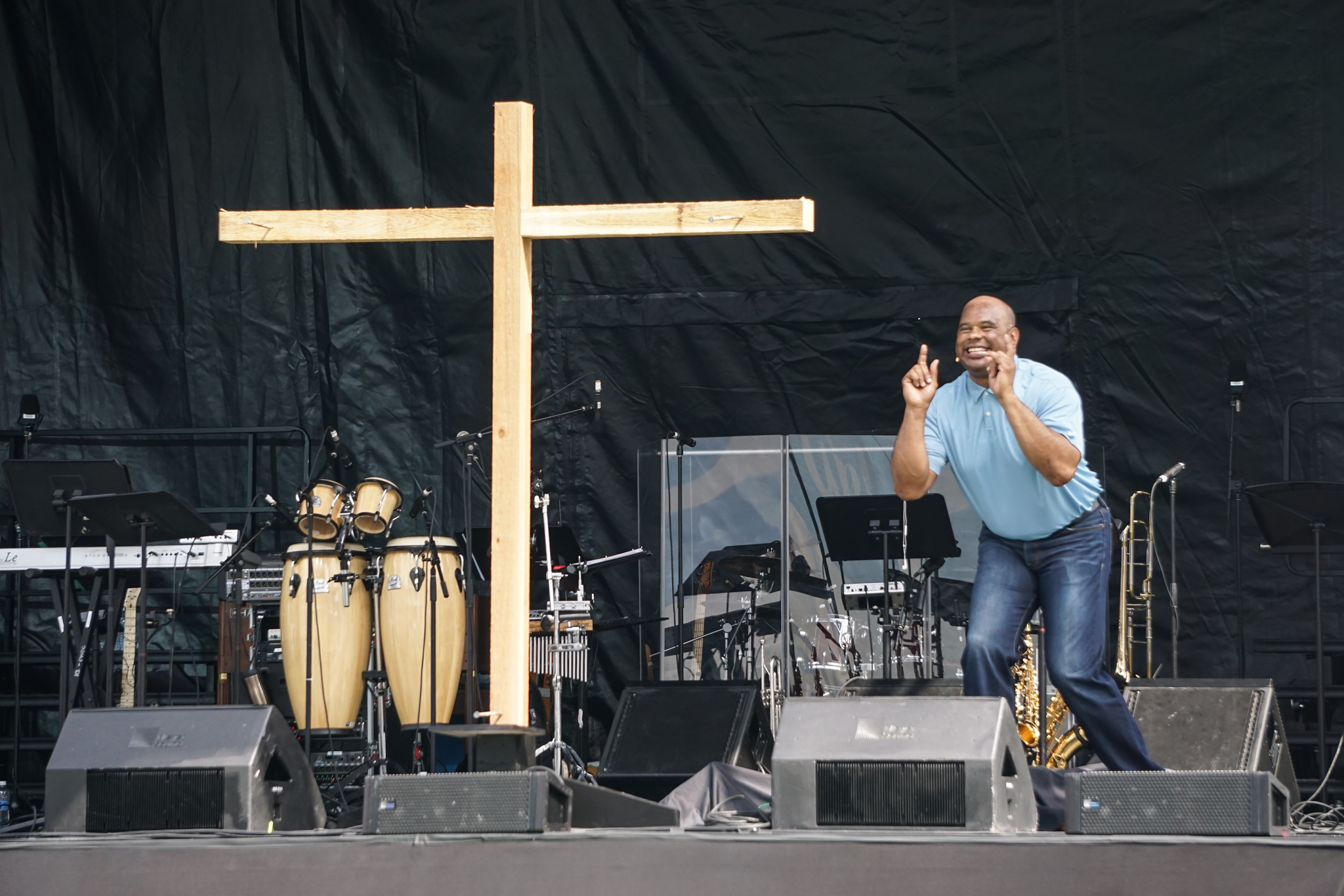 A man standing on stage with a cross behind him.