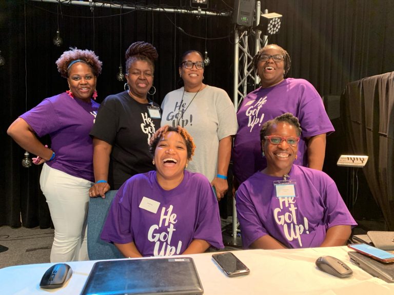 A group of people wearing purple shirts and smiling.