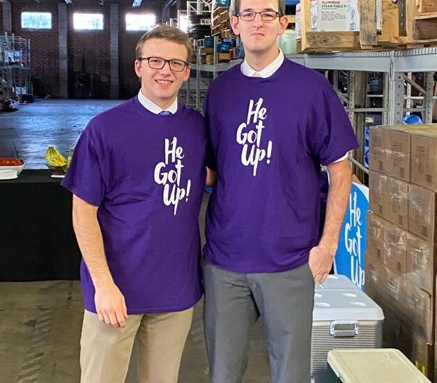 Two men wearing purple shirts standing next to each other.