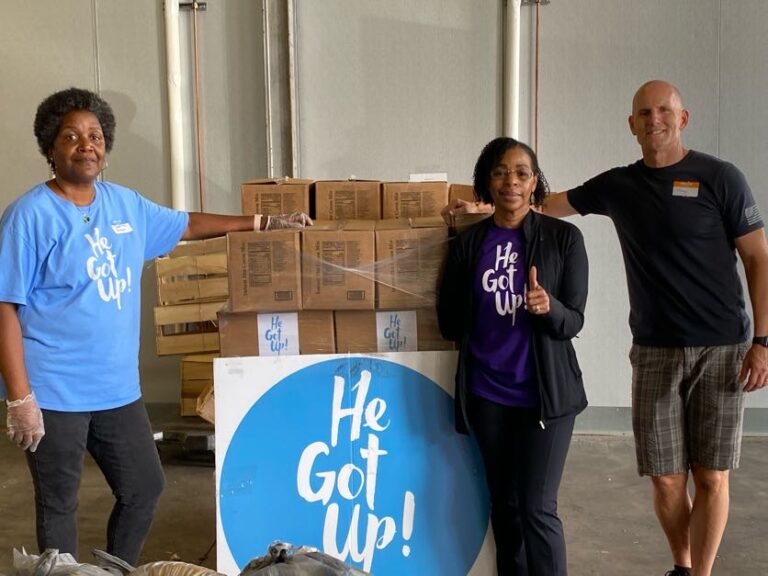 Three people standing in front of boxes and a sign.